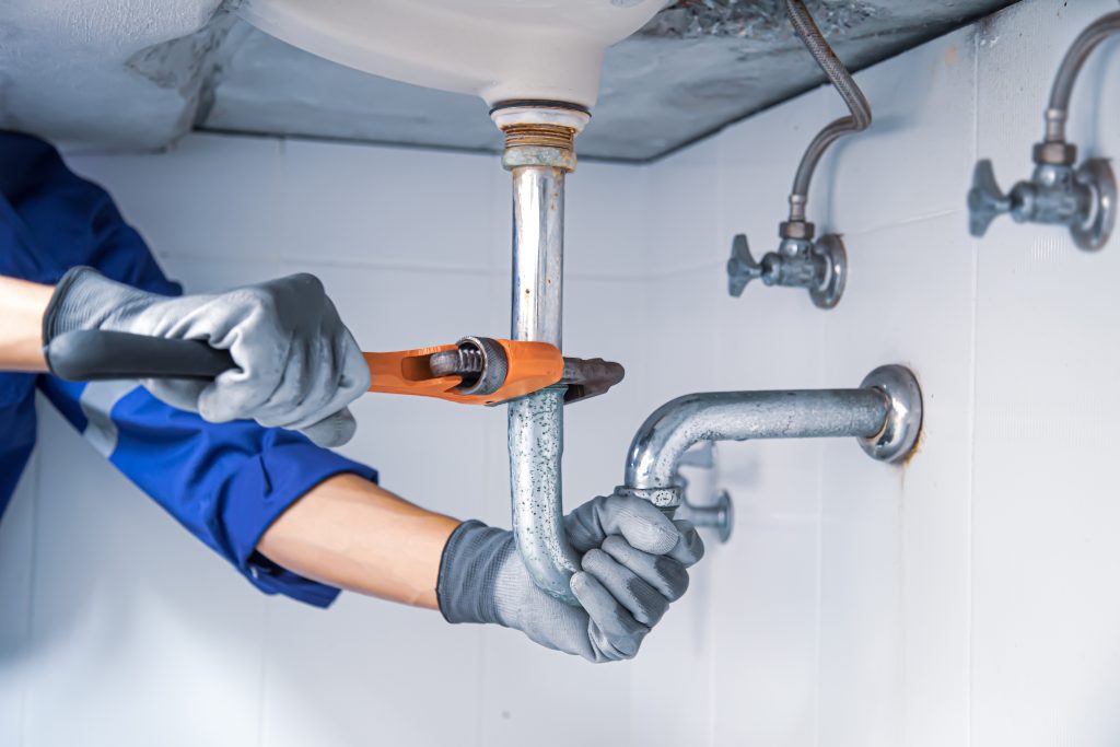 Home 2 Technician plumber using a wrench to repair a water pipe under the sink